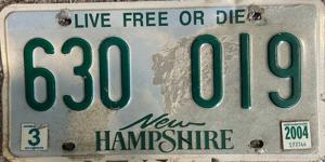 A New Hampshire license plate. The plate has a faint background image of a rocky landscape with dark green lettering. The lettering has a slogan ('Live free or die'), the registration number ('630 019') and the name of the state.