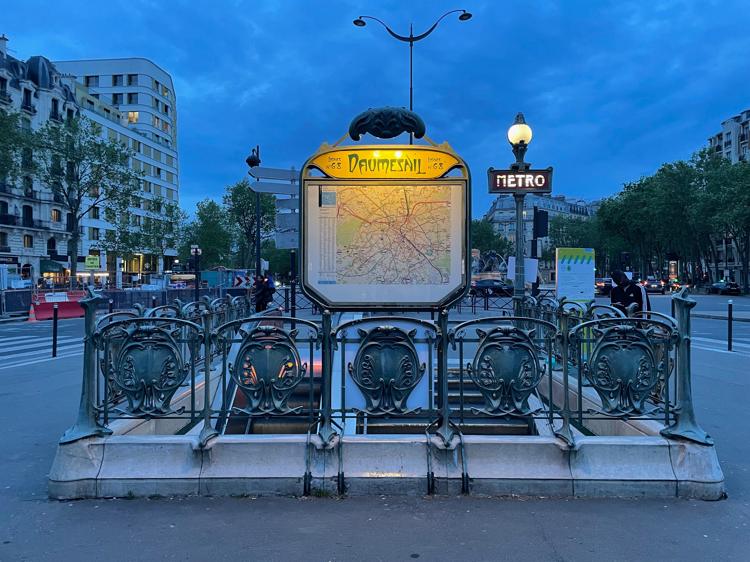 The entrance to the Bel-Air metro station. I’m standing on the opposite side of the road, looking across a pedestrian crossing into an open door on the other side. The interior of the station is lit up with a warm yellow light.